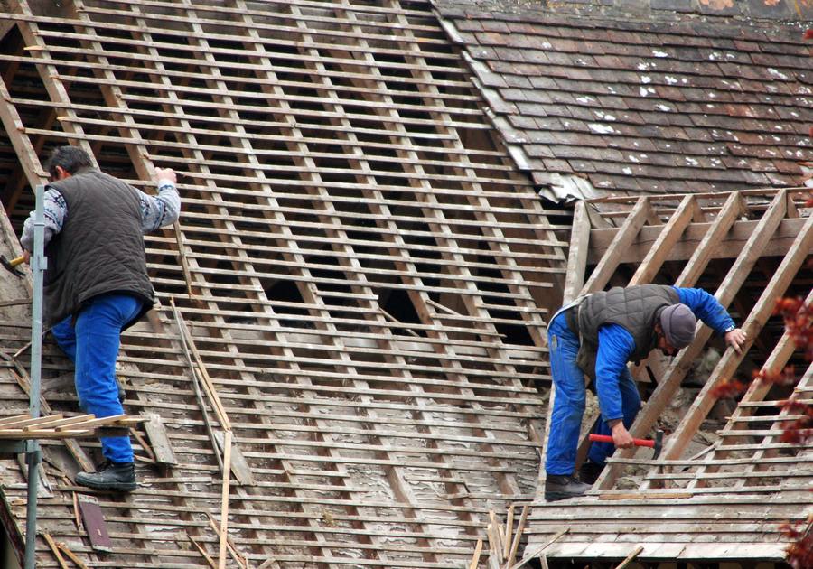 Zwei Dachdecker tragen bei einer Sanierung die alte Deckung ab, die Lattung liegt frei