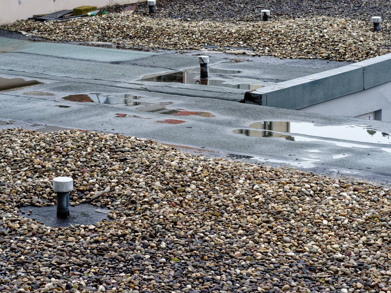 Flachdach mit stehendem Wasser, verrutschter Kiesschüttung und schadhafter Abdichtung